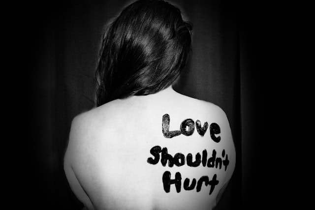 black and white image with 'love shouldn't hurt' painted on lady's back.
