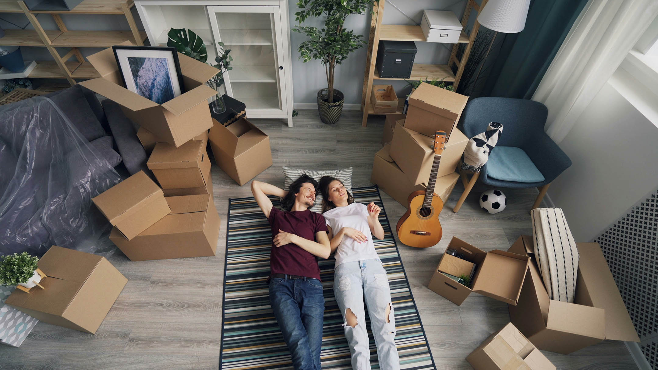 Young couple laying on a rug having just moved in surrounded by boxes.
